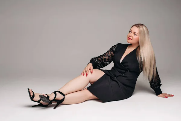 Attraktiv kvinna med långt blont hår i svart klänning ler på vit bakgrund — Stockfoto