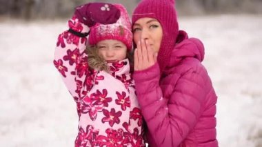 Anne ve kızı pembe bir aile kıyafetiyle soğuk bir kış günü öpüşüyorlar.