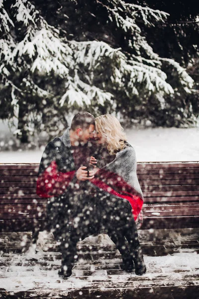 Couple in love sitting on bench and smiling in snowing forest. — Stock Photo, Image