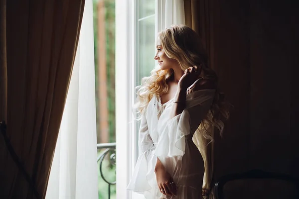 Nádherná nevěsta stojící blízko balkonu a dívá se do velkého okna. — Stock fotografie