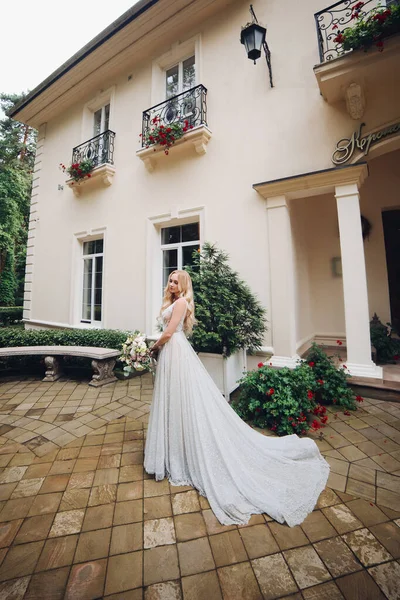 Sposa in abito da sposa perfetto posa contro casa di lusso con boquet di nozze . — Foto Stock