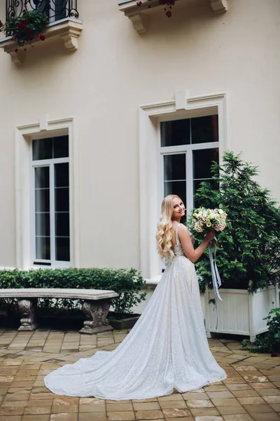 Sposa in abito da sposa perfetto posa contro casa di lusso con boquet di nozze . — Foto Stock