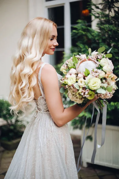 Sposa in abito da sposa perfetto posa contro casa di lusso con boquet di nozze . — Foto Stock