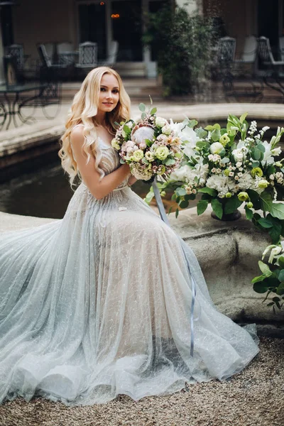 Elegante sensuale sposa bionda che tiene i fiori e posa alla macchina fotografica . — Foto Stock