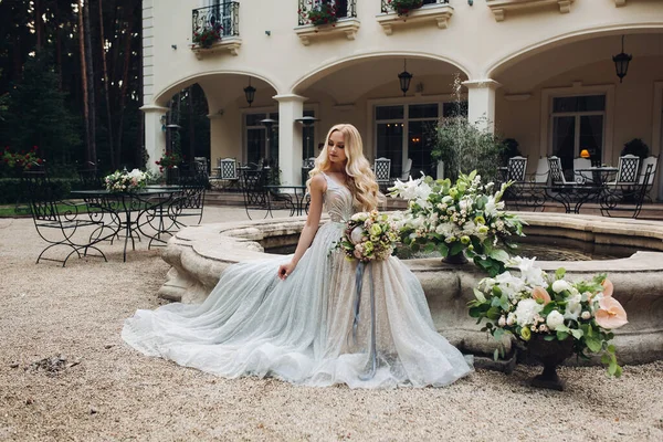 Elegante sensuale sposa bionda che tiene i fiori e posa alla macchina fotografica . — Foto Stock