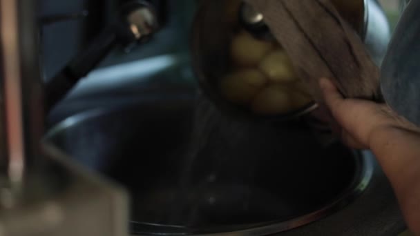 Eine Hausfrau gießt Wasser aus einem Topf einer gekochten Kartoffel in die Spüle — Stockvideo