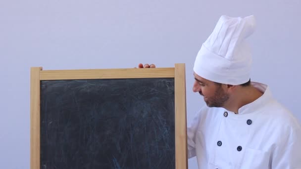 Bebaarde middelbare leeftijd chef-kok in witte toque en uniforme permanent op zoek naar de camera met copyspace op wit — Stockvideo