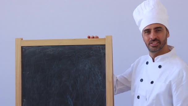 Chef barbudo de mediana edad en toque blanco y uniforme de pie mirando a la cámara con copyspace en blanco — Vídeos de Stock