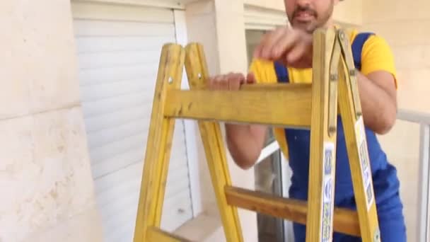 Будівельник з робочим одягом стоїть на драбині — стокове відео