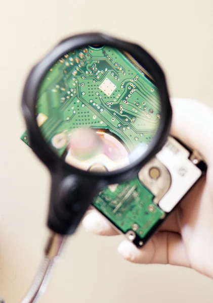 Mão segurando placa de circuitos eletrônicos sob lupa — Fotografia de Stock