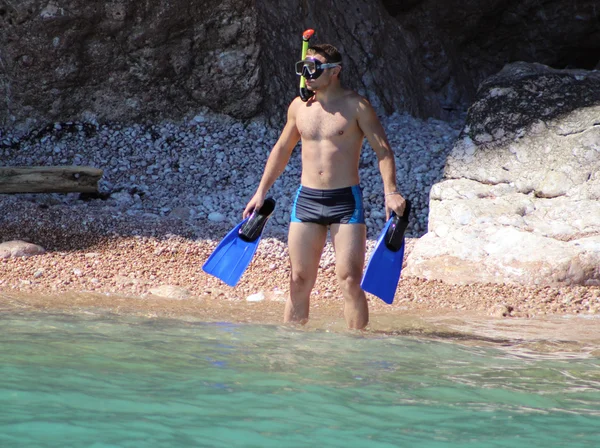 the person with a mask and flippers against the rock is going to plunge into the sea