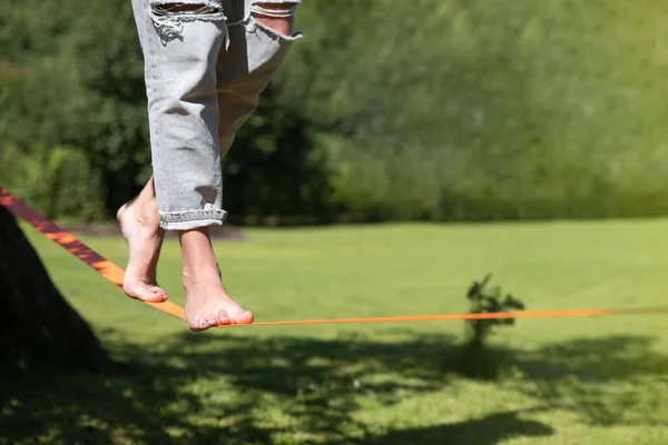在一个温暖的阳光明媚的夏天 在一个绿色的花园里 一个人踩着熊脚在松驰的训练平衡上行走 健康生活概念 免版税图库照片