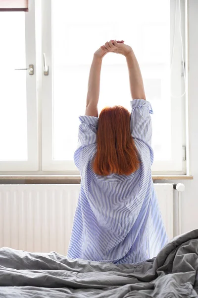 Mladá žena sedí na posteli a protahuje si paže po probuzení — Stock fotografie