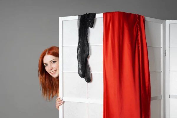 Young woman peeks from behind folding screen while undressing or changing clothes — 스톡 사진