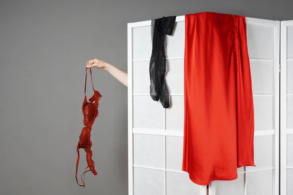 Hand hålla behå medan dold kvinna klär av sig bakom vikbar skärm — Stockfoto