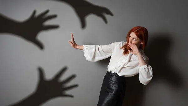 Terrified woman in defensive posture is attacked by shadows of hands — Zdjęcie stockowe