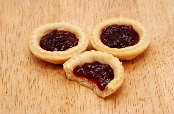 Three jam tarts, one with a bite taken, on a wooden table — Stock Photo, Image