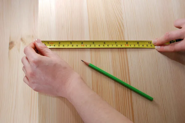 Twee handen meten een houten plank met een stalen meetlint — Stockfoto