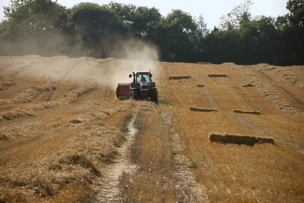Трактор и пресс-подборщик в поле во время сбора урожая — стоковое фото