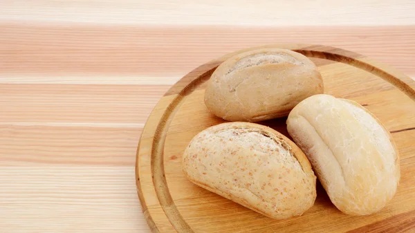 Three crusty petit pain on a bread board — Stock Photo, Image