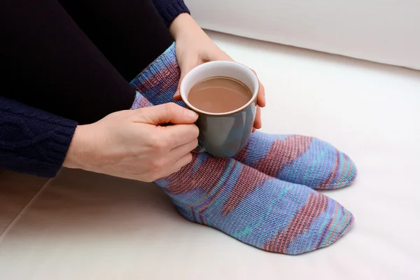 Woman holding a hot drink, wearing warm knitted socks — Stock Photo, Image