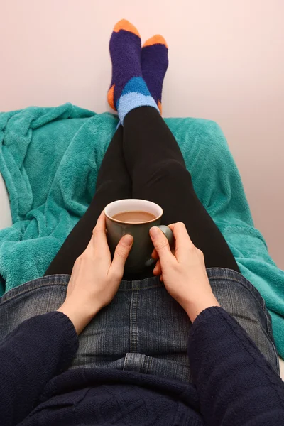 Woman holding a hot drink, relaxing with her feet up