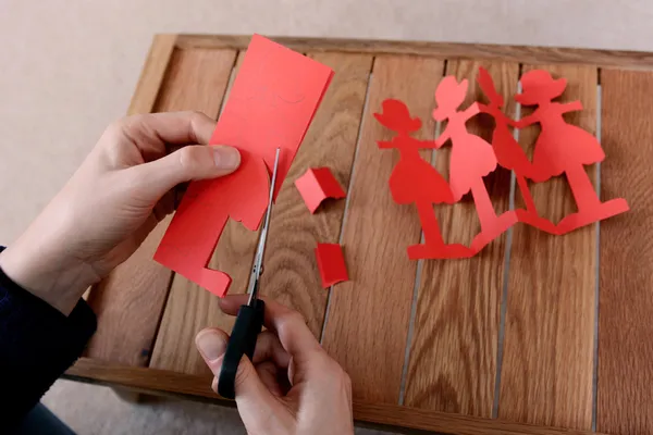 Taglio di una catena di bambole di carta rossa con le forbici — Foto Stock