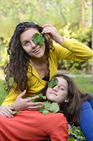 Dois bela adolescente se divertindo brincando no jardim com folhas verdes em seus olhos — Fotografia de Stock