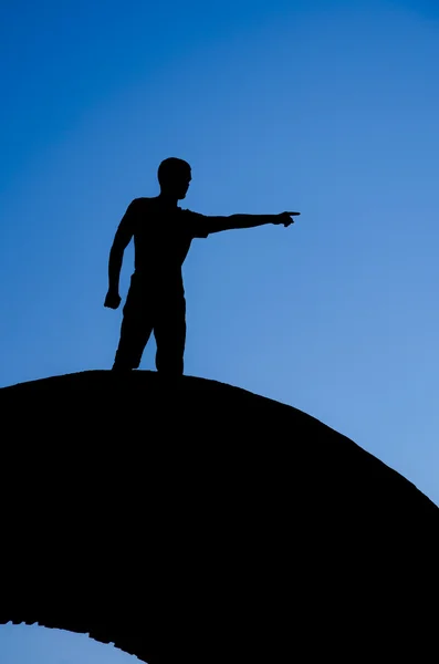 :un joven hombre de negocios guapo en acr y mano apuntando silueta sobre fondo de cielo azul — Foto de Stock