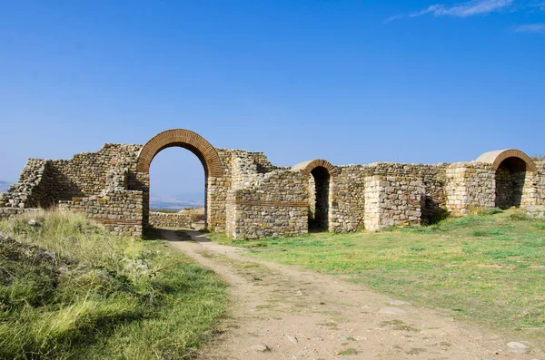 Ancient town ruins and path through arced stone gate — Stock Photo, Image