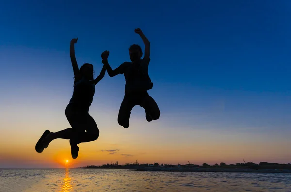 Silueta de niña y niño saltando en la puesta de sol de la playa — Foto de Stock