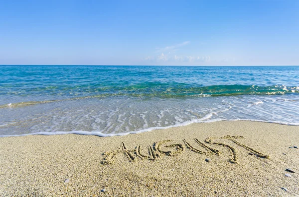 Palabra de AGOSTO dibujada en la arena de una playa — Foto de Stock