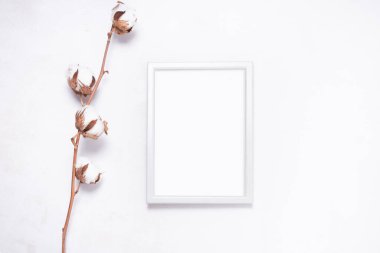 Fotoğraf çerçevesi beyaz ahşap üzerinde pamuk çiçek dallarıyla süslenmiş. 