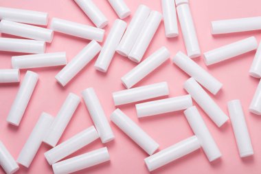 Pembe arka planda bir sürü beyaz plastik dudak parlatıcı tüpü var.