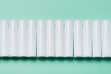 Mavi arka planda bir sürü beyaz plastik dudak parlatıcı tüpü var.
