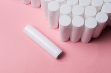 Pembe arka planda bir sürü beyaz plastik dudak parlatıcı tüpü var.