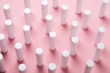 Pembe arka planda bir sürü beyaz plastik dudak parlatıcı tüpü var.