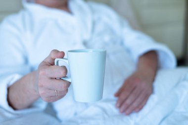 Man lies in bed with a mug in his hands. rest, laziness