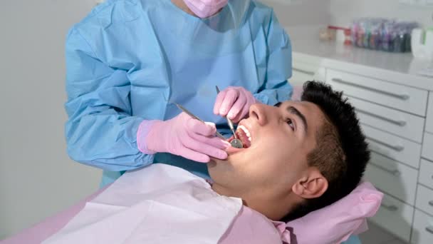 Dentista feminina examinando uma paciente com ferramentas na clínica odontológica. Médico fazendo tratamento dentário em dentes masculinos. — Vídeo de Stock