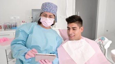 Diş hekimi ve hasta, arka plandaki tıbbi ekipmanlarla yapılan bir istişarede, tablet başvurusunda tedavileri yorumluyor..