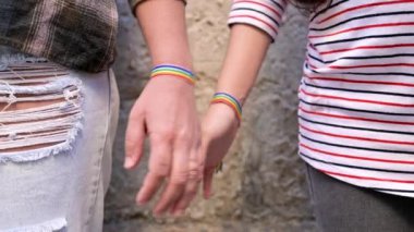 Yavaş çekim, mutlu lezbiyen çiftin el ele tutuşması gökkuşağı bilekliği takması, LGBT aşk konsepti.