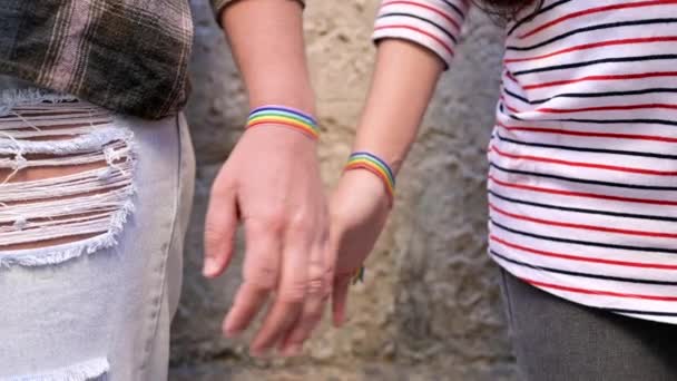 Mouvement lent, Gros plan d'un couple de lesbiennes heureuses tenant la main portant un bracelet drapeau arc-en-ciel, concept d'amour LGBT. — Video