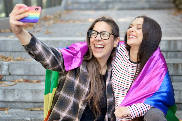 Alegre feliz lesbiana pareja holding lgbt bandera tomando un selfie al aire libre. —  Fotos de Stock