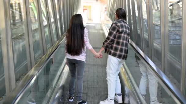エスカレーターでレズビアンカップル。両手を握っている二人の女性。同性愛とライフスタイルの概念. — ストック動画