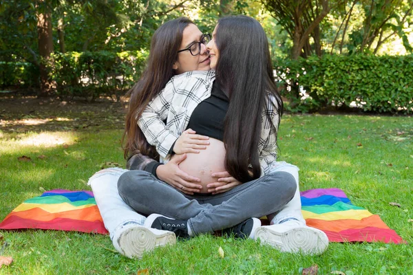 Ritratto di coppia lesbica incinta affettuosa con bandiera arcobaleno, rilassata al parco. Due amiche felici. Amore libero per lo stesso sesso. Relazione omosessuale. Orgoglio della comunità LGBT — Foto Stock
