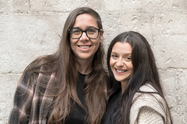 Дві молоді лесбіянки стоять біля кам'яної стіни, усміхнені, щасливі . — стокове фото