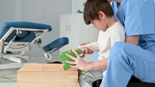 Fysiotherapeut verzorger helpen en spelen met een jongen met hersenverlamming gezondheidsprobleem, door het doen van oefeningen in revalidatie kliniek. Concept gehandicaptenzorg. — Stockvideo
