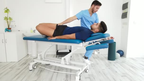 Revalidatietherapie. Fysiotherapeut werkt met jonge atleet mannelijke patiënt stretching in het revalidatiecentrum — Stockvideo