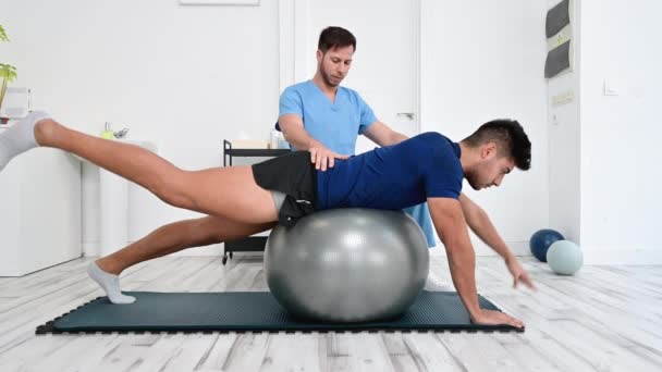 Fyzioterapeut pomáhá pohledný mladý pacient pro pilates cvičení s míčem. — Stock video