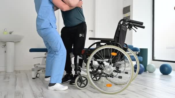 Man sjukgymnast hjälpa en patient med en neurologisk sjukdom att få upp från rullstol på rehabilitering sjukhus. — Stockvideo